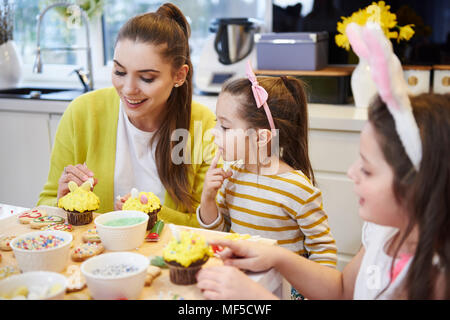 Mother with daughters decorating Easter cookies and muffins in kitchen Stock Photo