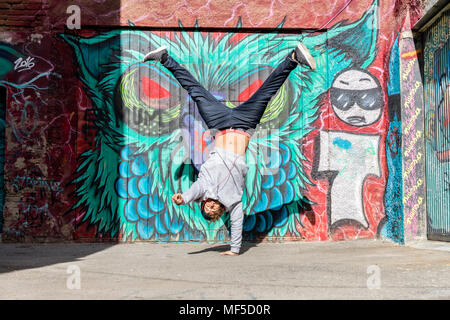 Young man with headphones doing handstand in front of graffiti Stock Photo