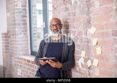 Portrait of smiling freelancer with tablet leaning against wall in a loft Stock Photo