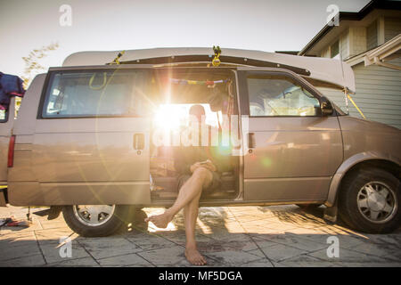 Barefoot man sitting in minivan in backlight using cell phone Stock Photo