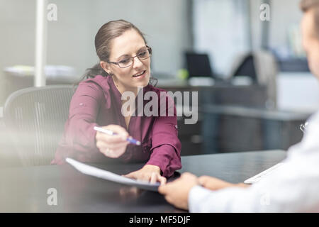 Woman showing contract to client at desk Stock Photo