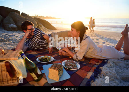 Happy couple having a picnic on the beach at sunset Stock Photo