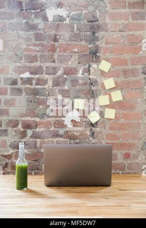 Glass bottle of green smoothie and laptop on wooden tabletop in a loft Stock Photo