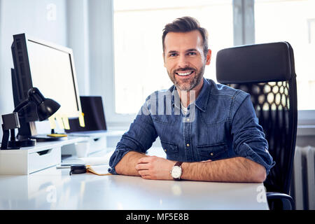 Portrait of smiling man sitting at desk in office Stock Photo