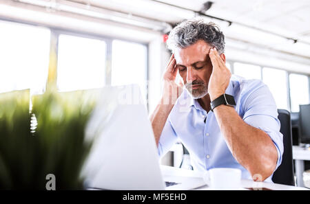 Stressed mature businessman sitting at desk in office with laptop Stock Photo