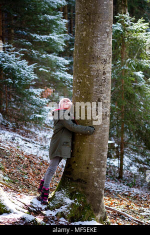 Girl hugging tree in forest in winter Stock Photo