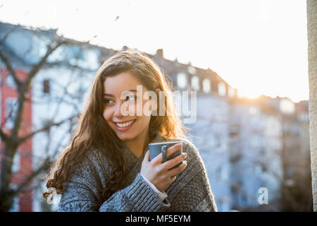 Portrait of laughing teenage girl with coffee mug on balcony at twilight Stock Photo