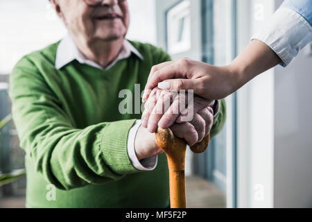 Close-up of woman holding senior man's hand leaning on cane Stock Photo