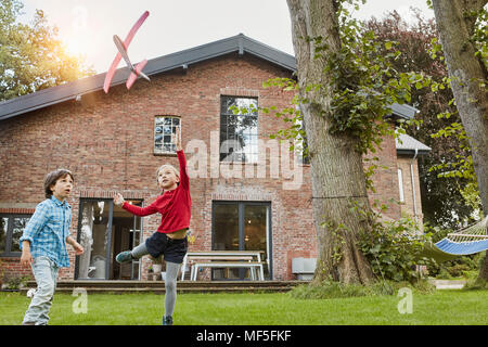 Two children playing with toy airplane in garden of their home Stock Photo