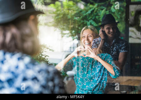 Beautiful young woman making a finger frame heart and smiling at her boyfriend through a window Stock Photo