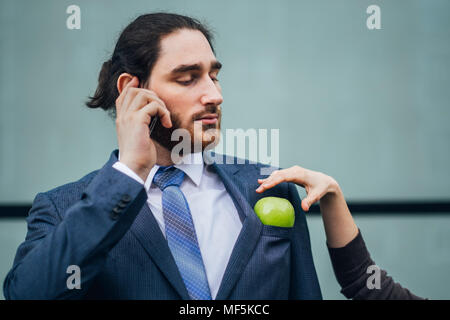 Businessman talking on cell phone and woman placing an apple in his jacket pocket Stock Photo