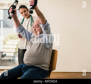 Young woman supporting senior man doing an arm exercise Stock Photo