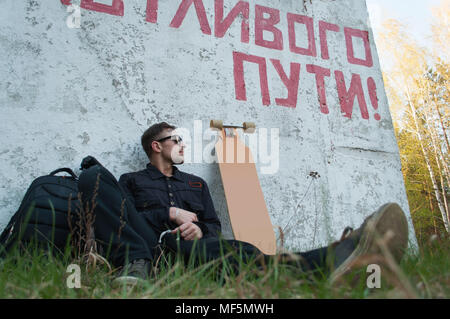 The guy is sitting next to the longboard, the concept of traveling on the longboard, the inscription on the wall of a Happy journey Stock Photo