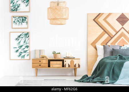 Green bedding on bed next to wooden cupboard in natural bedroom interior with gallery of posters Stock Photo