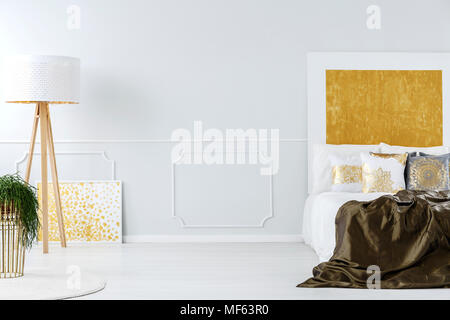 Luxurious white and golden minimalist bedroom interior with elegant furniture and a wooden tripod floor lamp Stock Photo