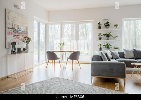 Fresh tulips in ceramic vase placed on a wooden table with two grey chairs standing in the corner of bright living room interior with decorations on c Stock Photo