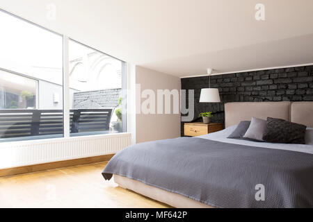 Windows in spacious bedroom interior with grey bedding on bed against black brick wall Stock Photo
