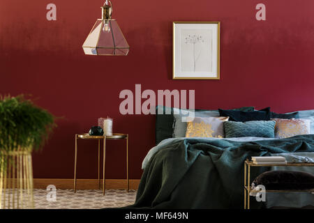 King-size bed with many pillows and green coverlet standing in burgundy room interior with poster on the wall Stock Photo