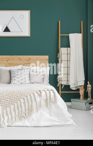 Beige blankets on bed and ladder in boho bedroom interior with poster on green wall Stock Photo