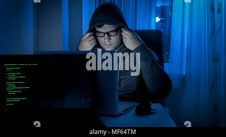 Portrait of male hacker working at night and wearing hood on head Stock Photo