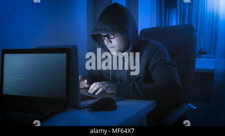 Portrait of concentrated hacker typing code of computer virus on laptop at night Stock Photo