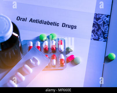 Diabetes drugs in packs and and medicine bottle placed on textbook. Green tablets and pink-white capsule pills. Diabetes mellitus type 2 therapy conce Stock Photo