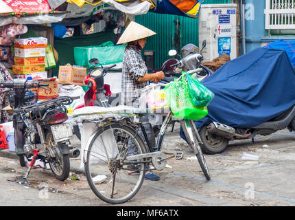 A Vietnamese woman wearing a conical hat loading bags of shopping on her bicycle in the Ton That Dam Street markets, Ho Chi Minh City, Vietnam. Stock Photo