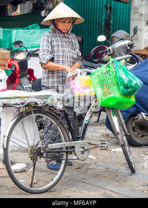 A Vietnamese woman wearing a conical hat loading bags of shopping on her bicycle in the Ton That Dam Street markets, Ho Chi Minh City, Vietnam. Stock Photo