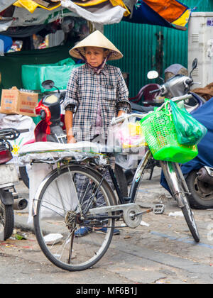 A Vietnamese woman wearing a conical hat loading bags of shopping on her bicycle in the Ton That Dam Street markets, Ho Chi Minh City, Vietnam. Stock Photo