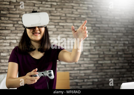 Happy smiling young woman playing game while getting experience using 360 VR headset glasses of virtual reality on bed at home