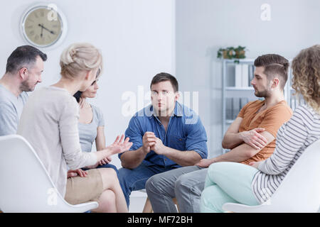 Sad, young man sitting in a bright office during a group meeting for gambling addicts Stock Photo