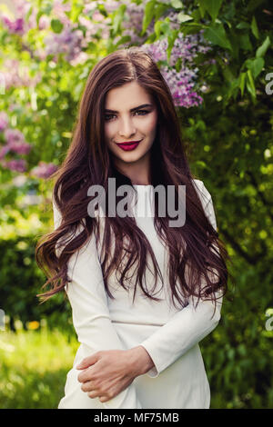 Beautiful woman brunette with long hair and makeup on lilac flowers background outdoors Stock Photo