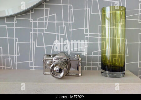 Sliver camera ornament with grenn vase on a sandstone fireplace with grey patterned wallpaper Stock Photo