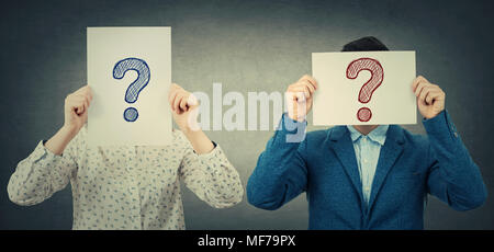 Businessman and businesswoman covering their faces using white paper sheets with drawn question marks, like a mask, for hiding identity. Isolated gray Stock Photo