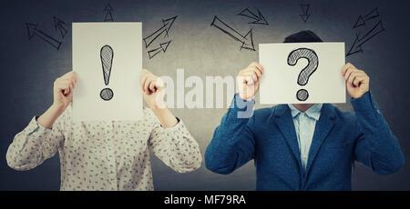 Businessman and businesswoman covering their faces using white paper sheets with drawn interrogation and exclamation marks, like a mask, for hiding id Stock Photo