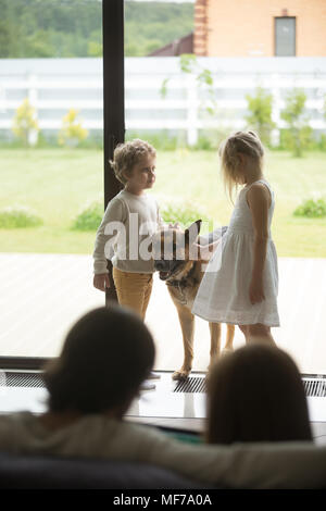 Kids playing with dog while parents relaxing at home, vertical Stock Photo