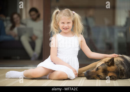 Smiling girl playing with dog outside house looking at camera Stock Photo