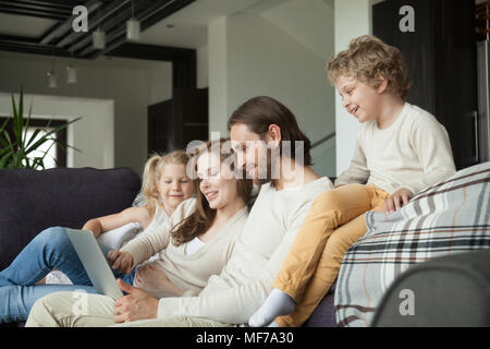 Happy family with children using laptop on couch at home Stock Photo
