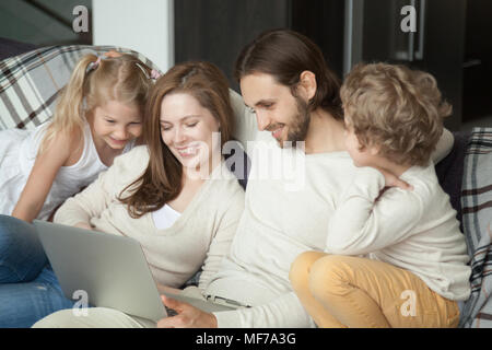 Smiling parents with kids having fun using laptop on sofa Stock Photo