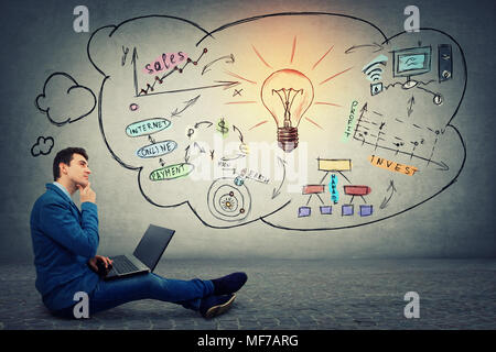 Thinking positive, young businessman sitting down on floor using laptop. Business network and idea concept. Light bulb sketch glowing over virtual sal Stock Photo