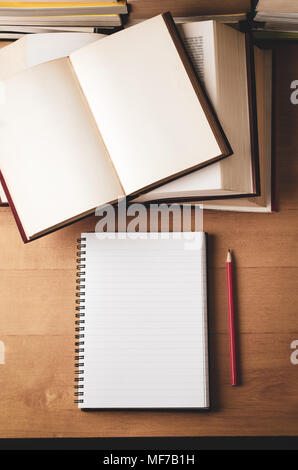 Overhead shot of study scene. Notebook opened on blank page, piles of textbooks and red pencil on wooden desk. Retro filtered in warm tones. Stock Photo