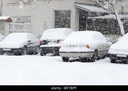 Back side of parked cars covered with snow while snowing, white building in background Stock Photo