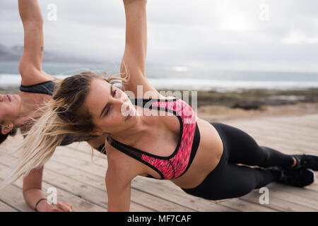 Toned women staying fit by the sea side with muscle strengthening excercises wearing beautiful fitness wear Stock Photo