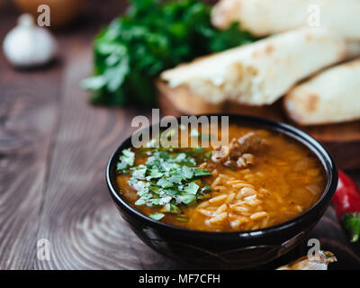 Traditional Georgian kitchen-soup Kharcho with meat, rice and fresh cilantro. Spicy soup Kharcho on wooden table with traditional bread Shotis Puri and vegetables. Selective focus. Copy space for text Stock Photo