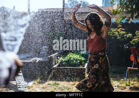 Water splashing on young woman in backyard Stock Photo