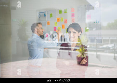 Portrait of smiling businesswoman in office with man working on board Stock Photo