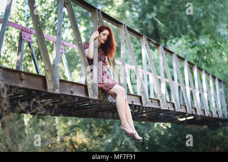 Spain, Andalusia, Granada. Beautiful red-haired woman sitting on a metallic bridge in nature. Lifestyle concept. Stock Photo