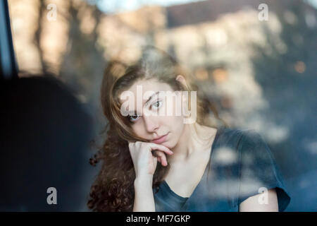 Portrait of pensive teenage girl behing windowpane Stock Photo