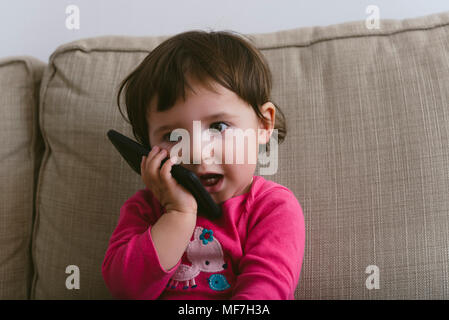 Baby girl talking on mobile phone at home Stock Photo
