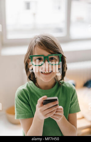 Portrait of smiling boy wearing pixel glasses holding cell phone Stock Photo